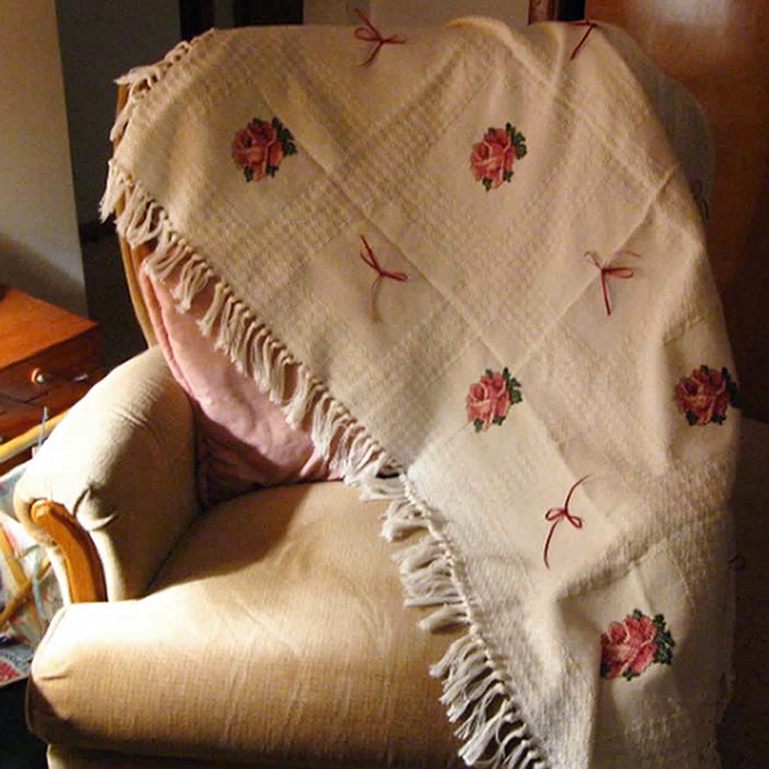 Cross stitched afghan with roses and bows on it.