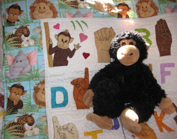 Handmade ASL/American Sign Language Quilt with stuffed monkey posing on top.